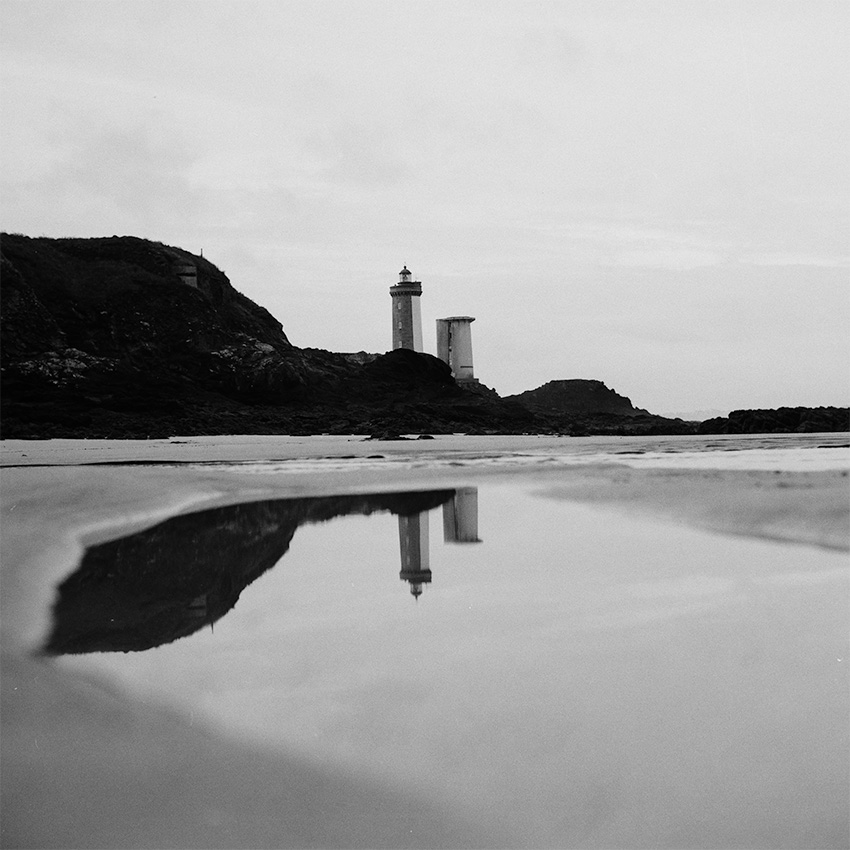 Le phare du petit minou se reflette dans un flaque sur la plage