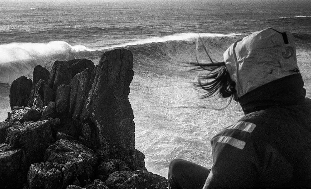 De grosses vagues viennent se fracasser sur la cote Brestoise, une femme les regarde avec ses cheveux dans le vent