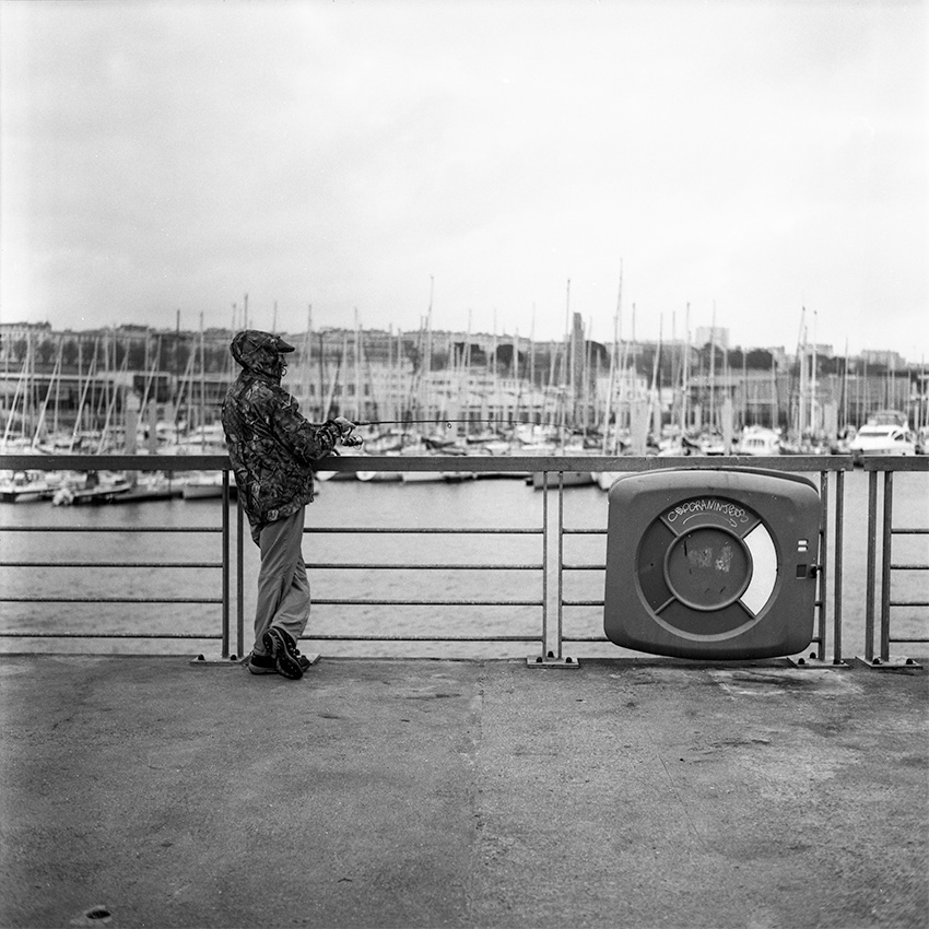 Un pêcheur Brestois avec à capuche devant les bateaux de la marina du château